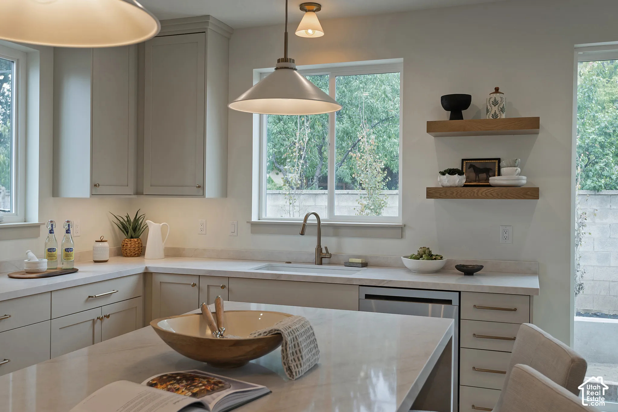 Kitchen featuring light-toned cabinetry, stone-finish countertops, an undermount sink with a metallic faucet, floating wood shelves, and pendant lighting