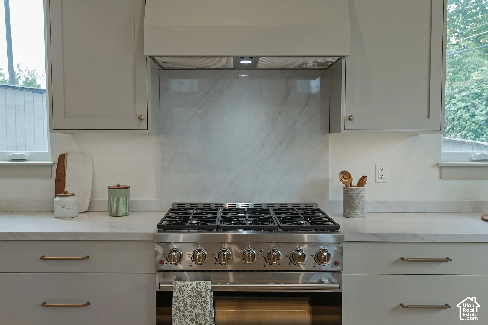 Stainless steel gas range with six burners, neutral-toned cabinetry, matching slab backsplash, and quartz countertops with metallic finish hardware