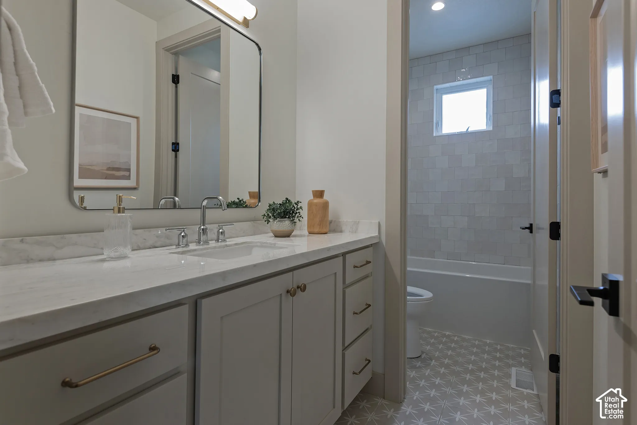 Neutral-toned vanity with a stone-finish countertop, undermount sink, metallic hardware, and an arched wall-mounted mirror, featuring a tub-shower combination with square tile surround and geometric patterned flooring