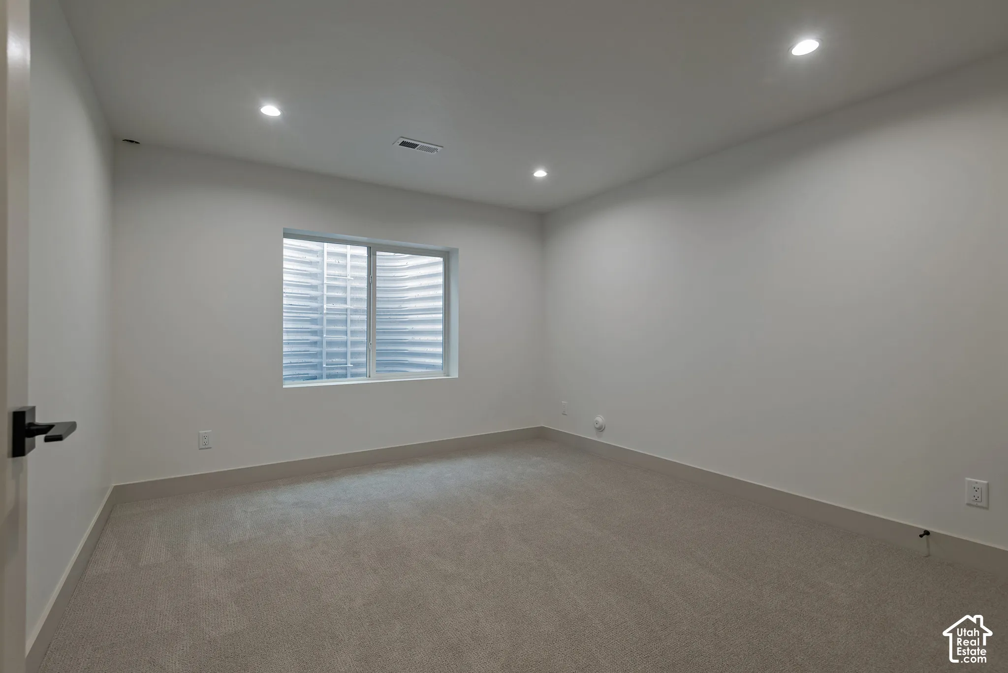 Neutral-toned room featuring wall-to-wall carpeting, recessed ceiling lighting, and a sliding window with a window well