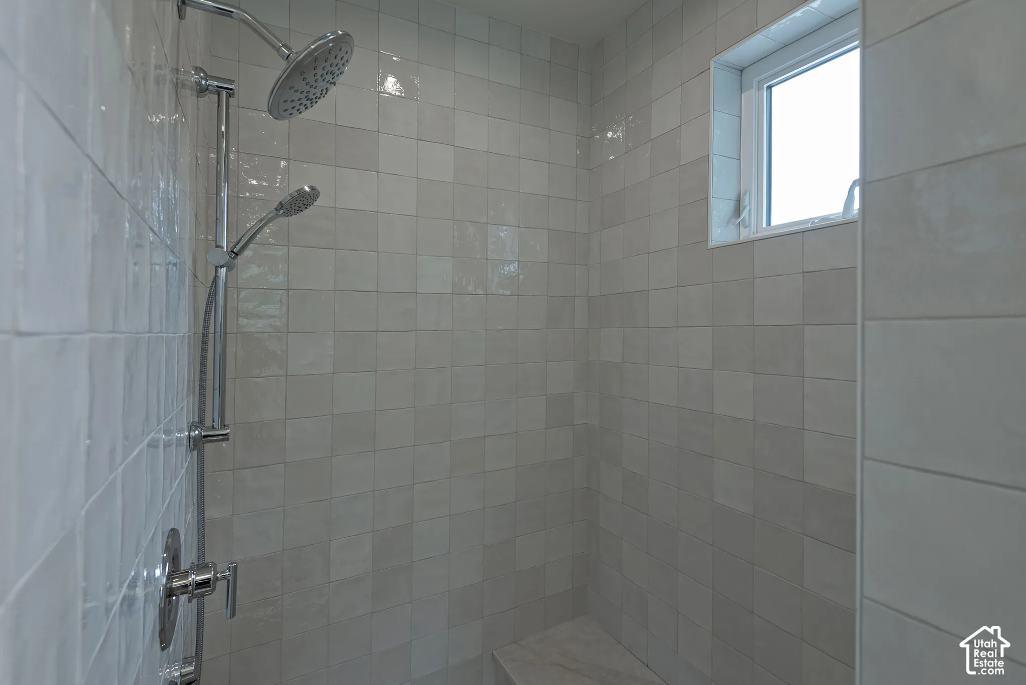 Shower enclosure featuring square gloss-finish wall tile, dual shower heads with chrome finish, integrated stone-topped bench, and a rectangular transom window