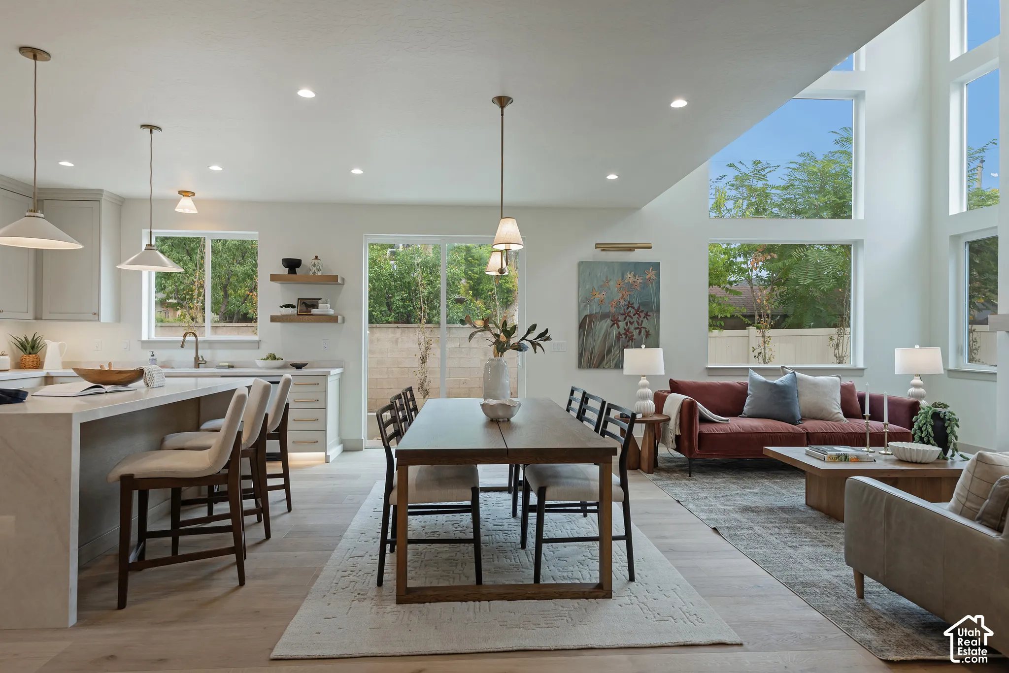 Open-concept kitchen and living area featuring high ceilings, oversized windows, light-toned wood-finish flooring, and a stone-topped kitchen island