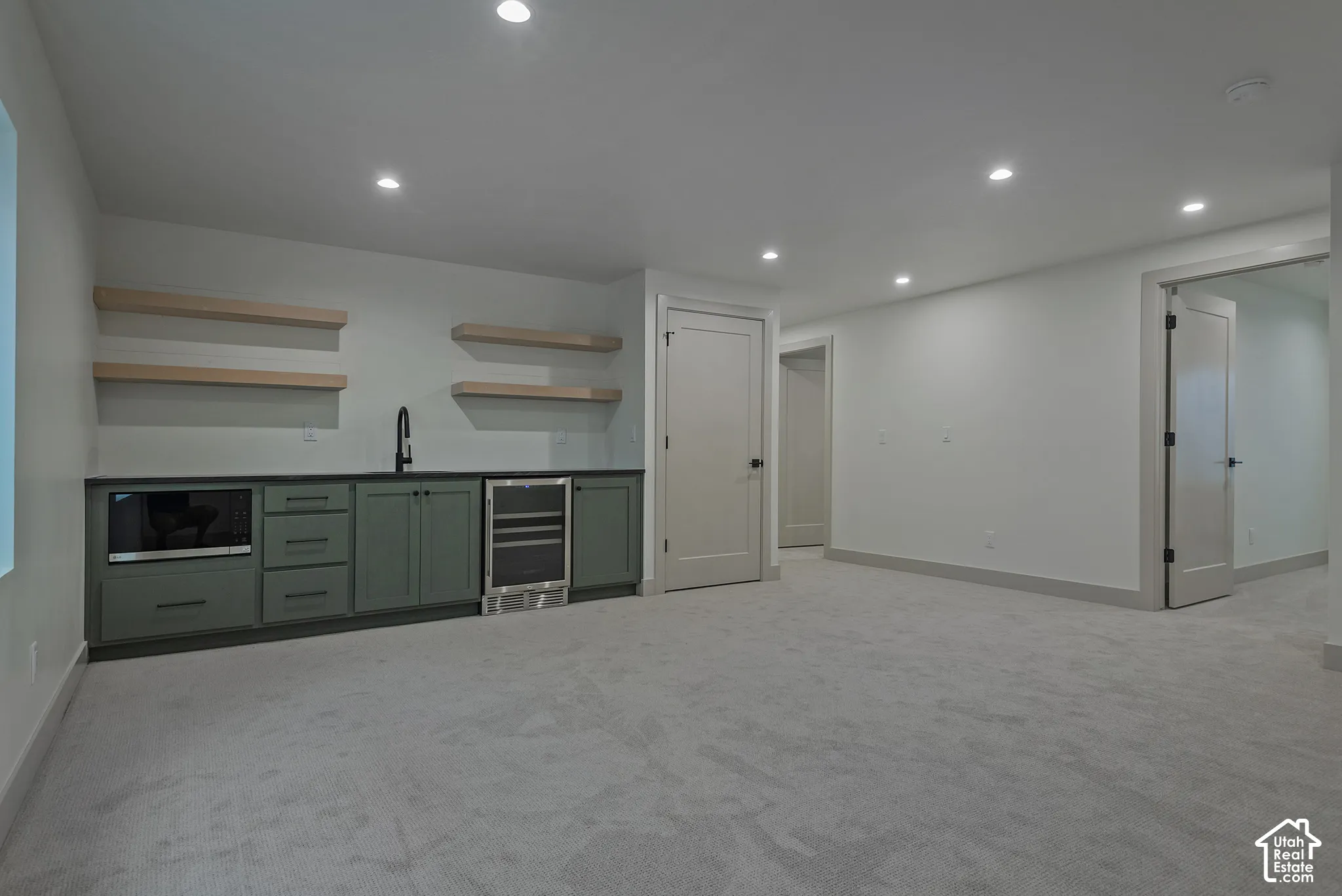 Wet bar area featuring sage-toned cabinetry, a dark countertop, integrated microwave, under-counter beverage refrigerator, and wood-finish floating shelving