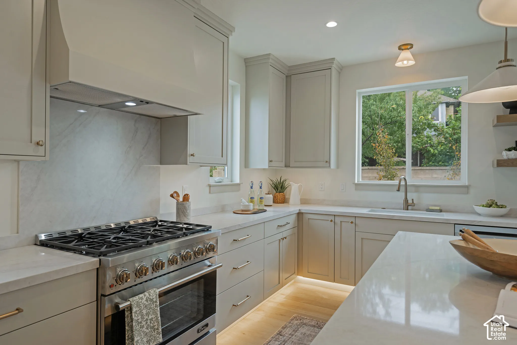 Kitchen featuring shaker-style cabinetry, professional-grade gas range with matching hood, stone-finish slab backsplash, quartz countertops, and under-cabinet lighting