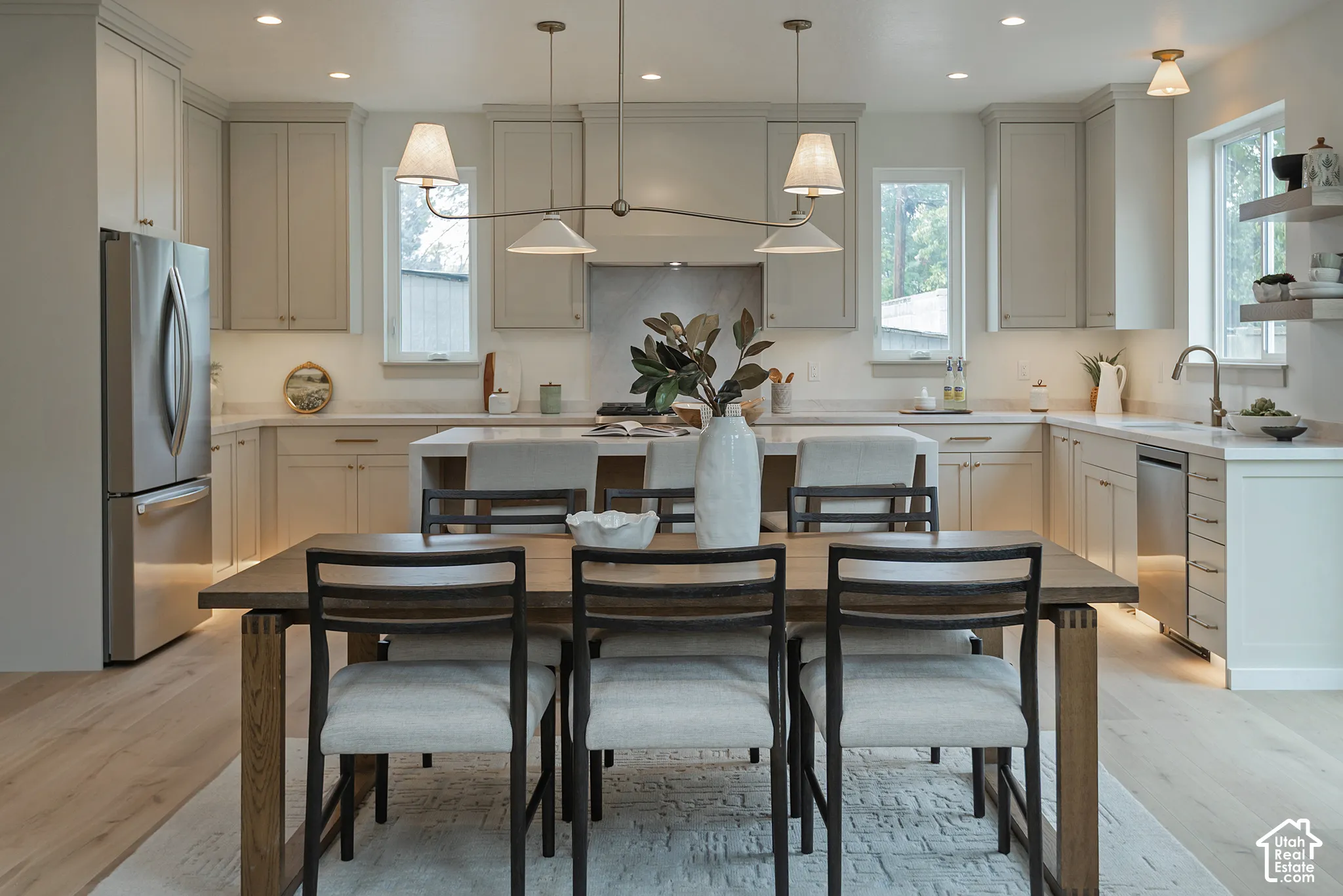 Kitchen featuring custom cabinetry, light-toned countertops, stainless steel appliances, wood-finish flooring, and multi-light overhead pendant lighting