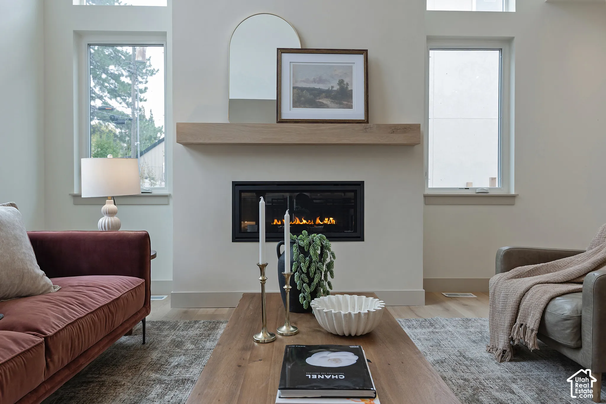 Linear fireplace featuring a minimalist black frame and natural wood floating mantel, flanked by tall rectangular windows with wood-finish flooring