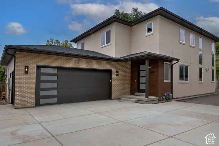 Multi-story exterior featuring a brick and stucco facade, wood-paneled entry surround, multi-panel garage door with frosted glass inserts, and concrete driveway