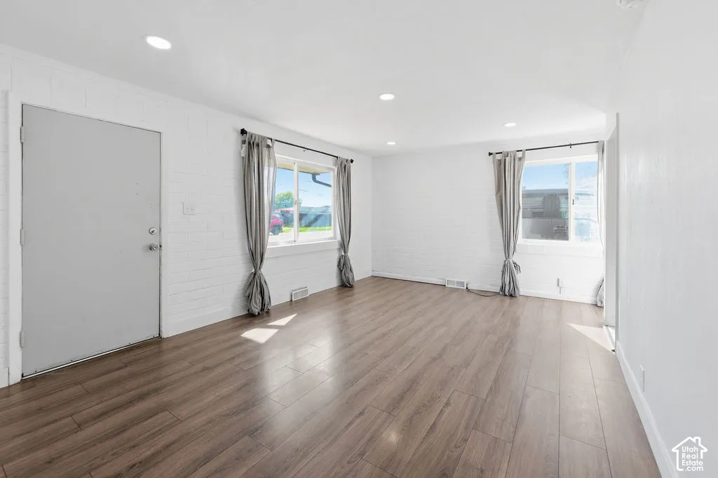 Interior featuring wood-finish flooring, white-painted brick walls, and recessed ceiling lighting