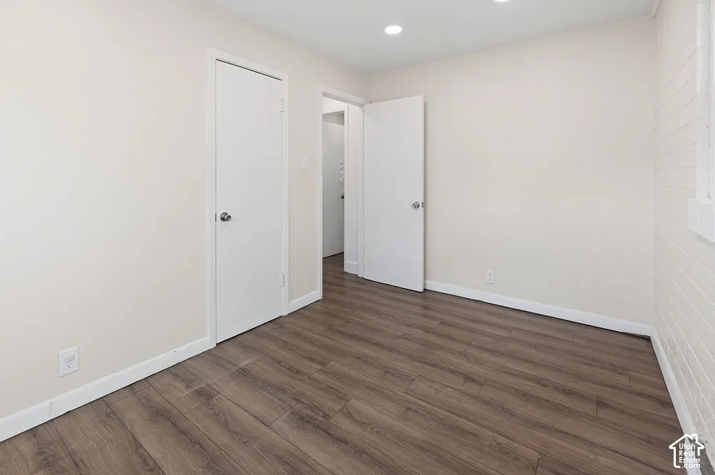 Interior room featuring wood-finish flooring, painted brick wall detailing, recessed ceiling lighting, and solid-core interior doors