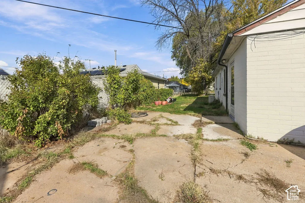 Exterior side yard featuring a light-colored masonry wall, a concrete patio area, and chain-link perimeter fencing