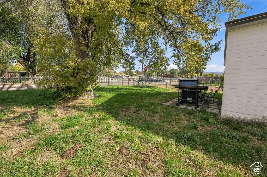 Outdoor space featuring a lawn, mature trees, and metal perimeter fencing