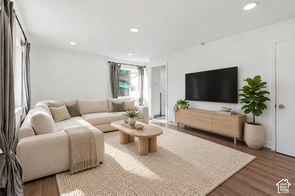 Living space featuring wood-finish flooring, recessed lighting, and a painted brick accent wall