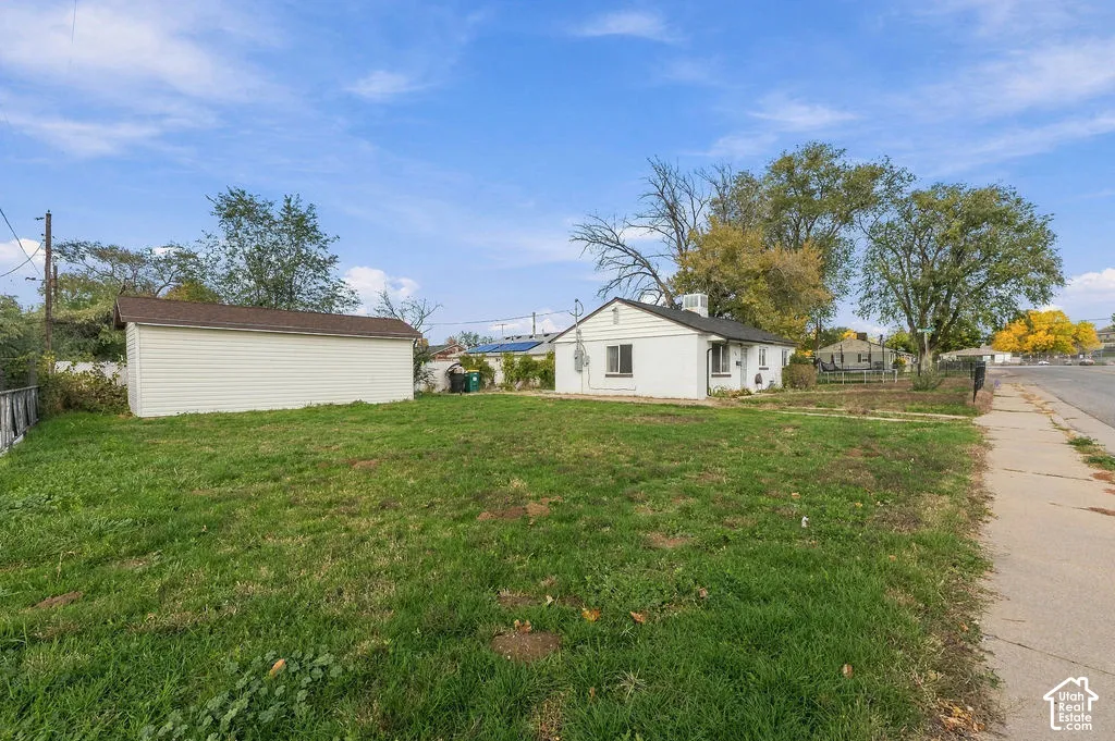Exterior featuring a detached garage, white siding, and a spacious grass yard