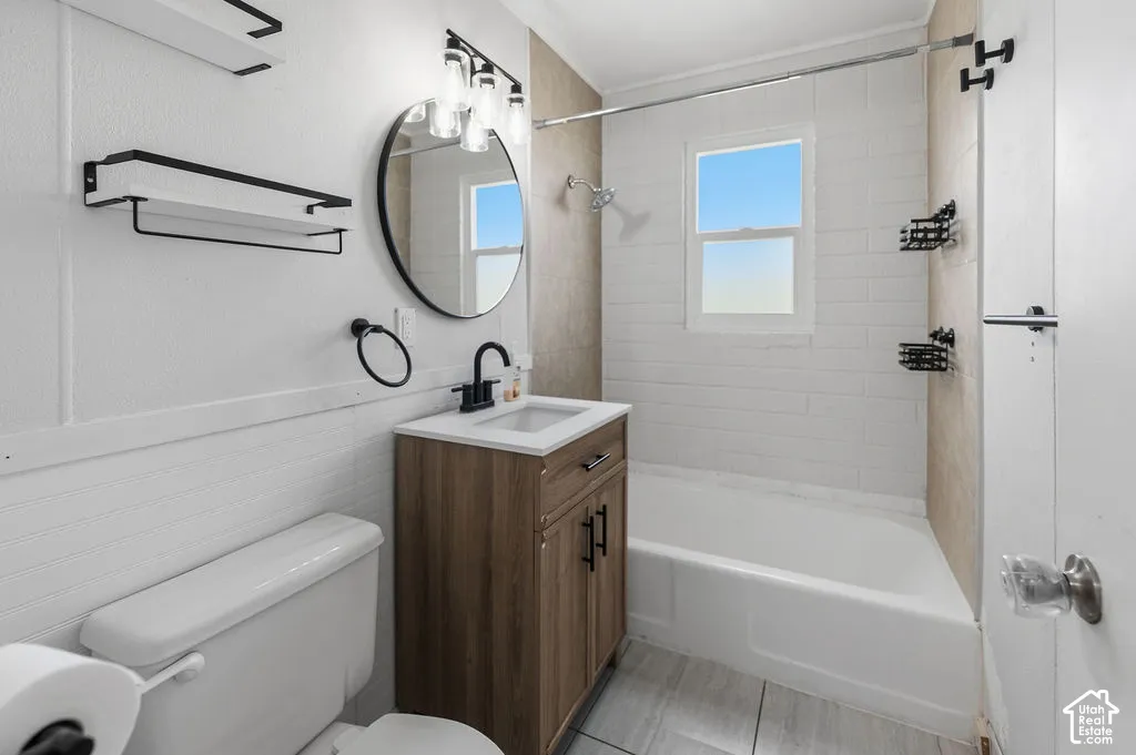 Bathroom featuring a wood-finish vanity with a rectangular sink, matte black fixtures, a circular wall mirror, and a tub-shower combination with light-toned tiled surrounds