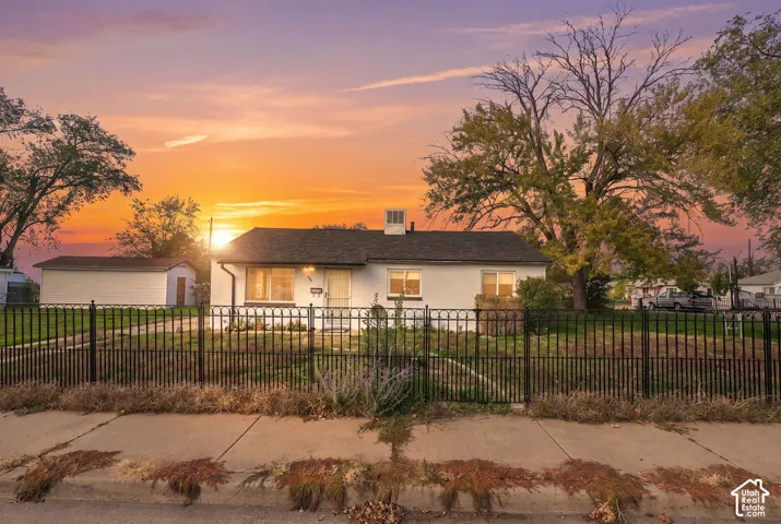 Single-story residence featuring a painted brick exterior, shingled roof, metal fencing, and an auxiliary detached structure