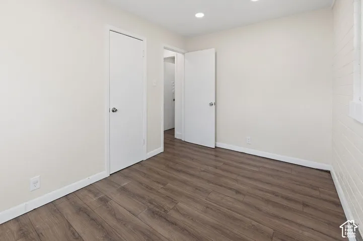 Interior room featuring wood-finish flooring, painted brick wall detailing, recessed ceiling lighting, and solid-core interior doors