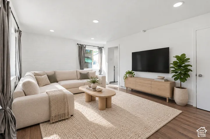 Living space featuring wood-finish flooring, recessed lighting, and a painted brick accent wall