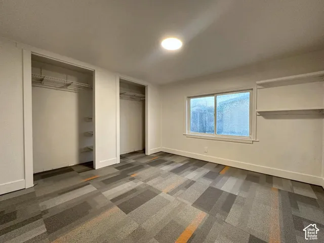 Room featuring patterned carpeted flooring, two reach-in closets with wire shelving, a horizontal sliding window, and built-in wall shelving