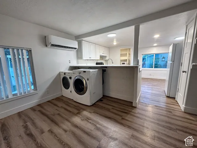 Kitchen featuring white cabinetry, wood-finish flooring, a wall-mounted climate control unit, and a pass-through counter