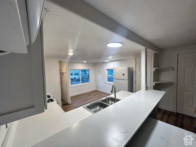 Kitchen featuring a breakfast bar, dual-basin stainless steel sink with a high-arch faucet, wood-finish flooring, and recessed ceiling lighting