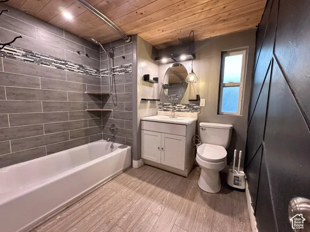 Full bathroom featuring gray rectangular tile shower surround with mosaic accent banding, white vanity cabinet with a integrated sink, wood-plank ceiling, wood-finish flooring, and black geometric wall paneling