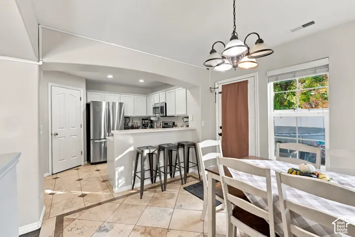 Kitchen featuring white cabinetry, stainless steel appliances, a breakfast bar, and tile flooring with decorative inserts
