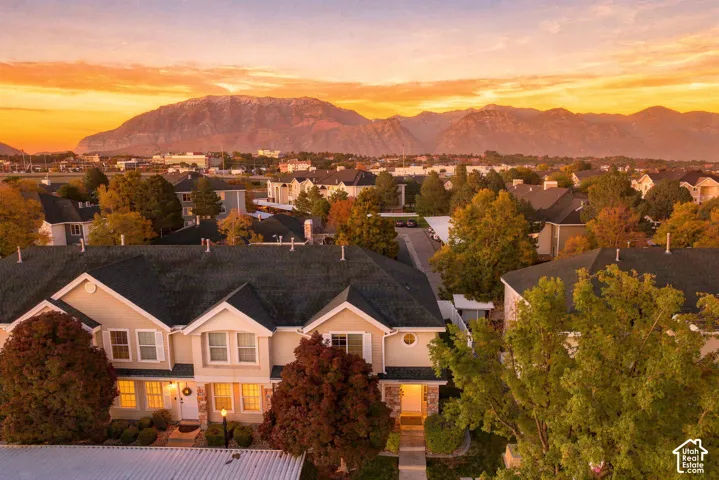 Multi-level exterior featuring light-toned siding, stone veneer accents, pitched shingle roofing, and mature landscaping against a mountain backdrop