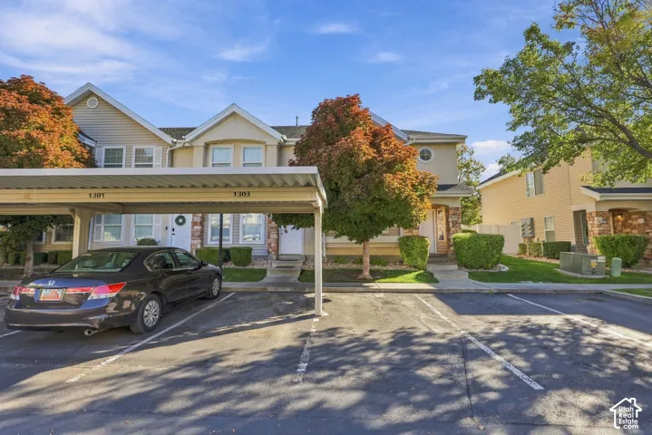 Exterior featuring a multi-story facade with vinyl siding, stone masonry accents, an attached covered carport, and mature landscaping