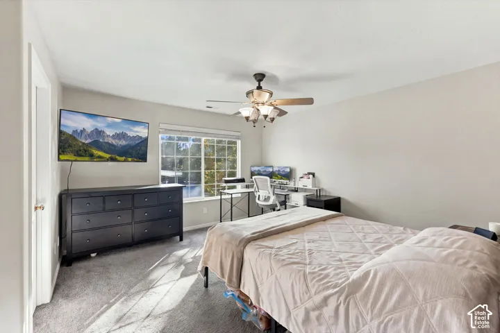 Neutral-toned bedroom featuring neutral carpeting, a multi-pane sliding window, and a ceiling-mounted light fixture with a fan