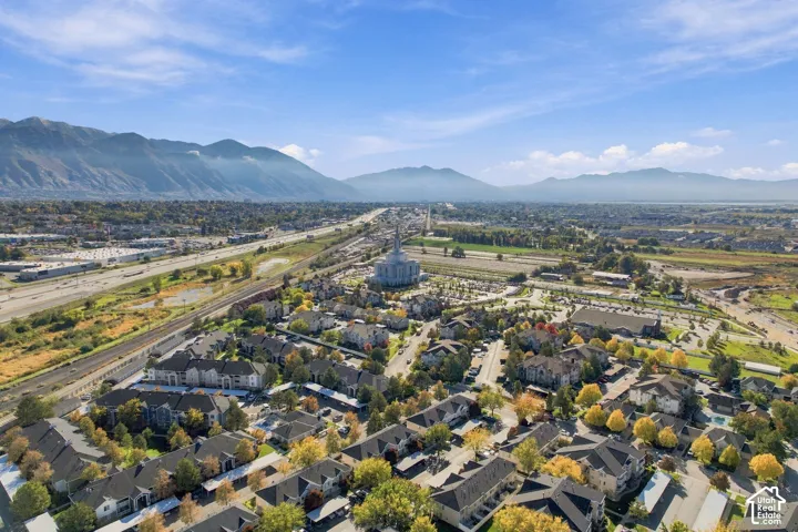 Aerial perspective featuring multi-story residential buildings, mature landscaping, paved surface parking, and a backdrop of mountain scenery