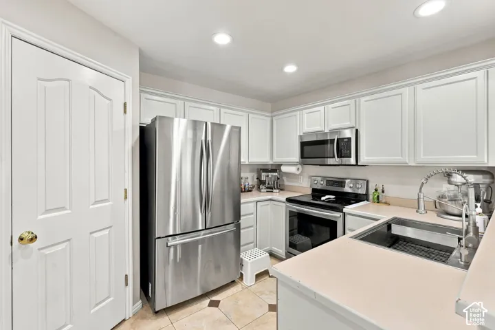 Kitchen featuring white cabinetry, stainless steel appliances, recessed lighting, and tile flooring with decorative inserts