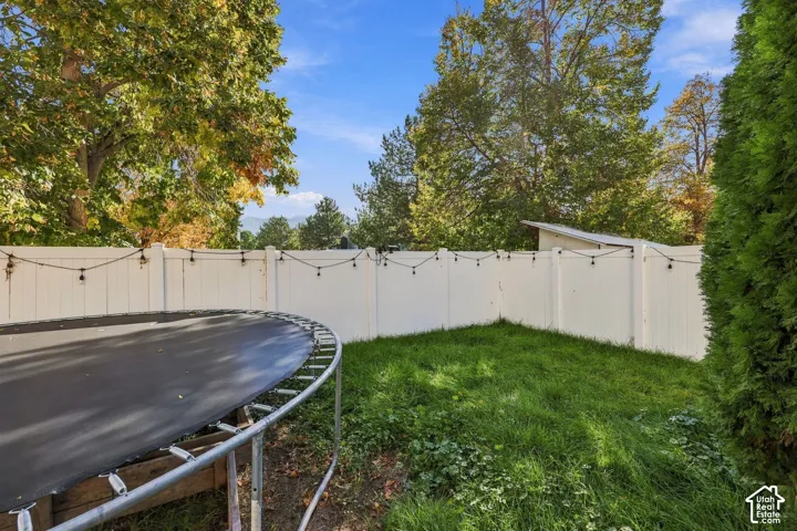 Backyard featuring a white vinyl privacy fence, mature trees, and mountain backdrop