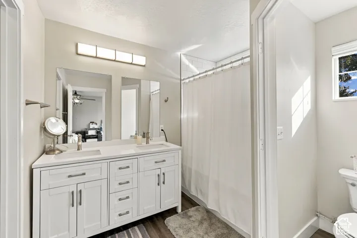 Dual-sink vanity with white cabinetry, light-toned countertop, and rectangular undermount sinks, paired with frameless vanity mirrors, multi-light bar fixture, and wood-finish flooring