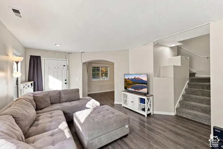 Living area featuring wood-finish flooring, an arched entryway, recessed lighting, and carpeted staircase