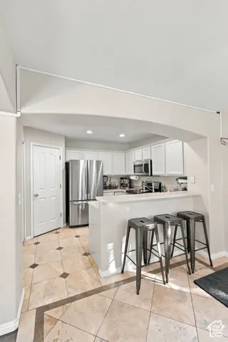 Kitchen featuring an arched entryway, stone-tile flooring with decorative inserts, a peninsula with a stone countertop, white cabinetry, and stainless-steel appliances