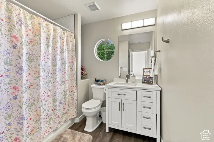 Bathroom featuring wood-finish flooring, white vanity with rectangular sink, wall-mounted four-light fixture, mirror, and a circular accent window