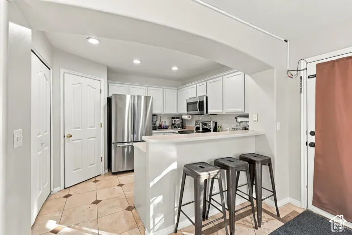 Kitchen featuring white cabinetry, stainless steel appliances, stone-finish flooring with decorative inlays, recessed lighting, and a peninsula with a breakfast bar