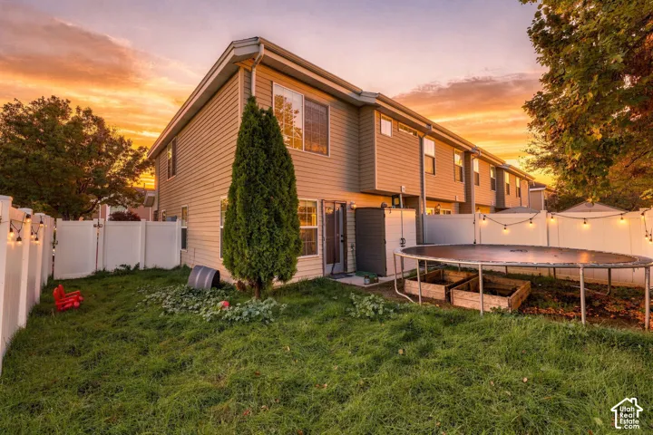 Two-story exterior featuring light-colored horizontal siding, a fenced perimeter, and raised garden beds