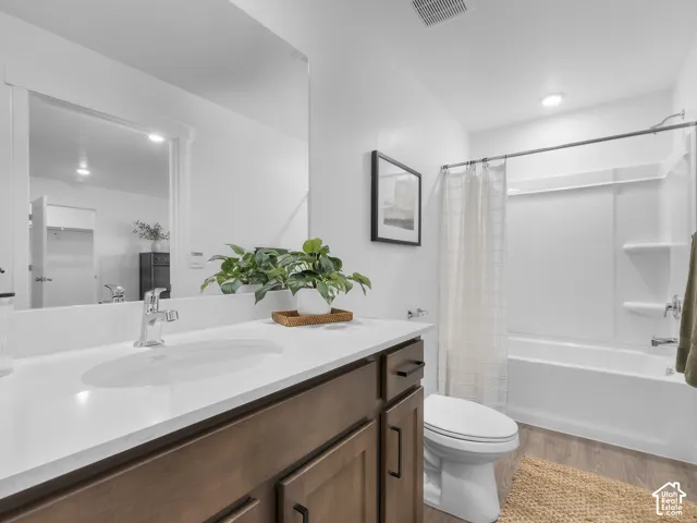 Bathroom featuring a wood-finish vanity with a white countertop and oval undermount sink, large wall-mounted mirror, and a full-length tub and shower combination with a composite surround