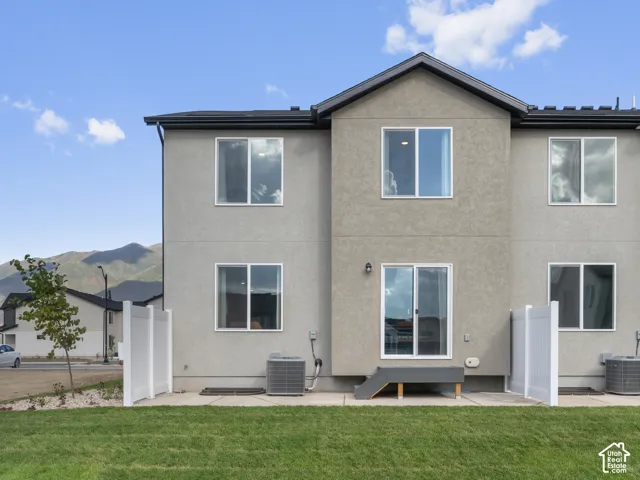 Two-story stucco exterior featuring a sliding glass door, a concrete rear patio, white vinyl fencing, and mountain scenery