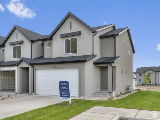 Two-story exterior featuring light-toned stucco siding, a multi-gabled roofline, a two-car garage, and concrete walkway