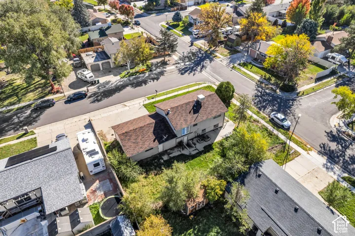 Aerial perspective of a multi-level residence on a corner lot featuring a gabled roofline, concrete driveway, and established landscaping