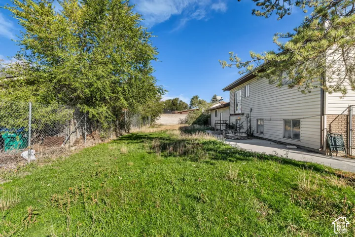 Side yard featuring horizontal lap siding, concrete patio, chain-link fencing, and mature trees
