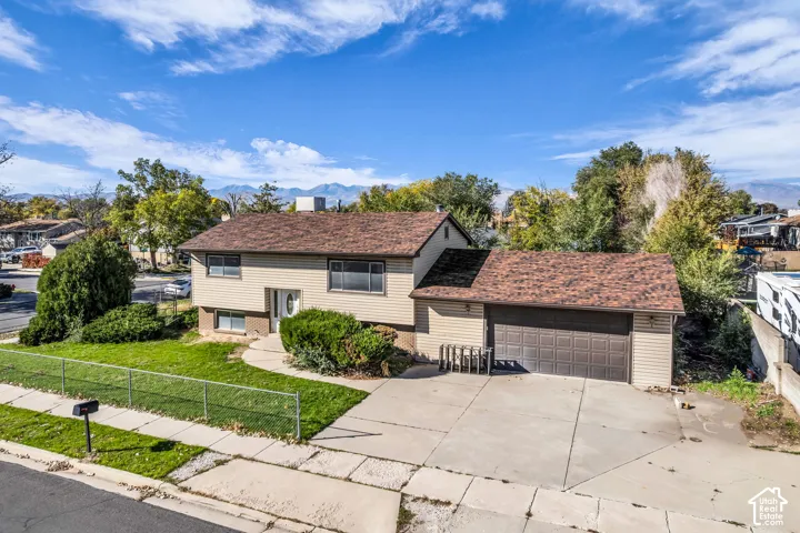 Split-level residence featuring horizontal siding, asphalt shingle roof, attached two-car garage, concrete driveway, and chain-link perimeter fencing