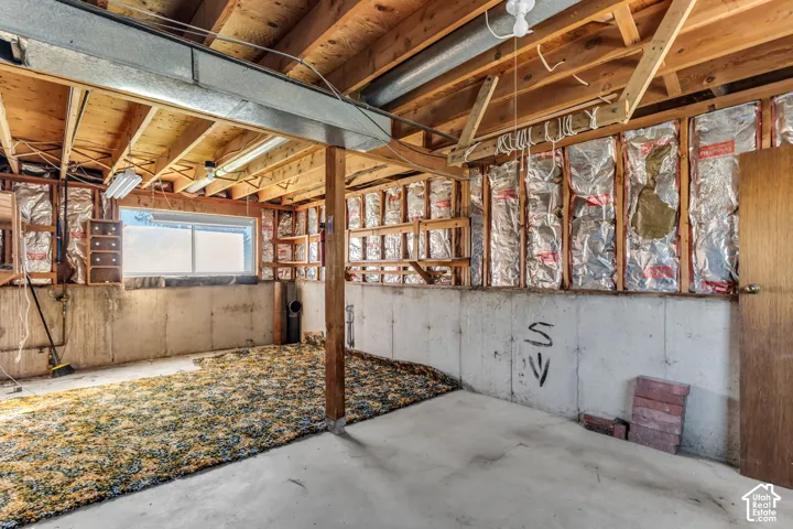 Unfinished space featuring exposed ceiling joists, concrete foundation walls, reflective insulation panels, and a single-pane horizontal window
