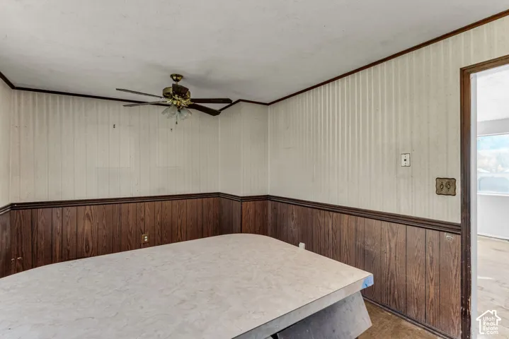 Interior space featuring wood-paneled wainscoting, textured wallpaper, and a ceiling fan with integrated lighting