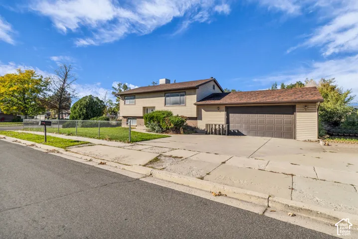 Split-level exterior featuring horizontal siding, a multi-paneled garage door, an expansive concrete driveway, and a chain-link fenced yard