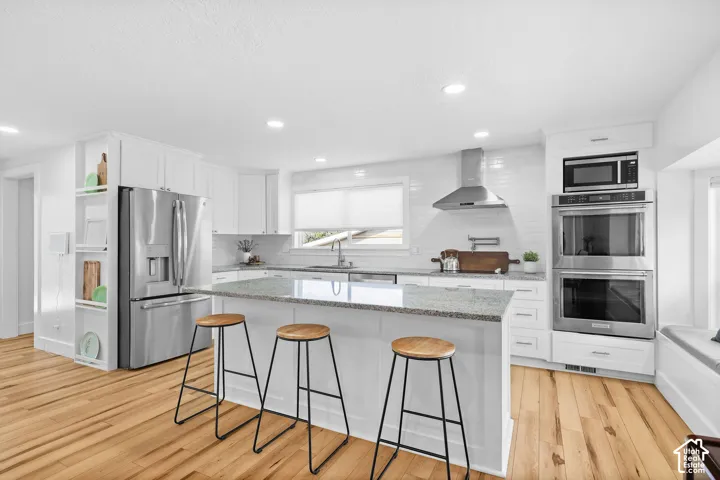 Kitchen featuring a central island with stone countertop, stainless steel double wall ovens, stainless steel range hood, recessed lighting, and wood-finish flooring