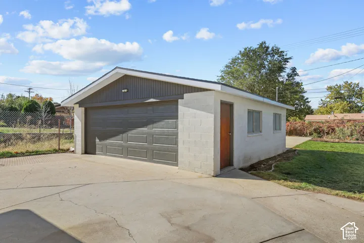Detached two-car garage featuring concrete block construction, a dual-panel overhead door, and an integrated side-entry access door, complemented by an expansive concrete driveway