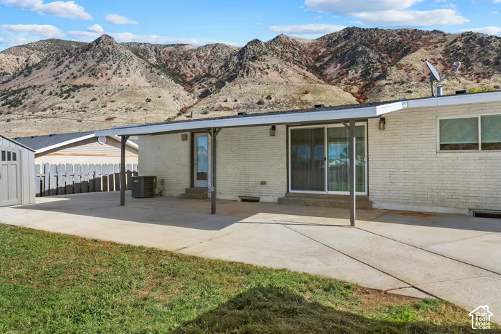 White brick exterior featuring a covered concrete patio, sliding glass doors, and expansive mountain scenery
